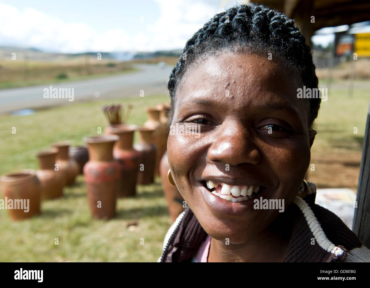 Portrait of a happy working African woman with beautifully threaded hair selling handmade clay pottery on roadside in rural South Africa. Stock Photo