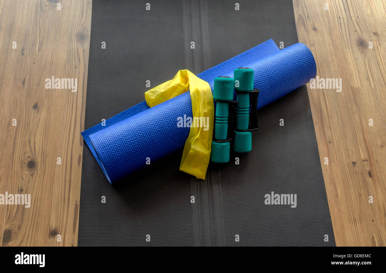 Hand weights, resistance band, and yoga mat on black foam mat on wooden floor background Stock Photo