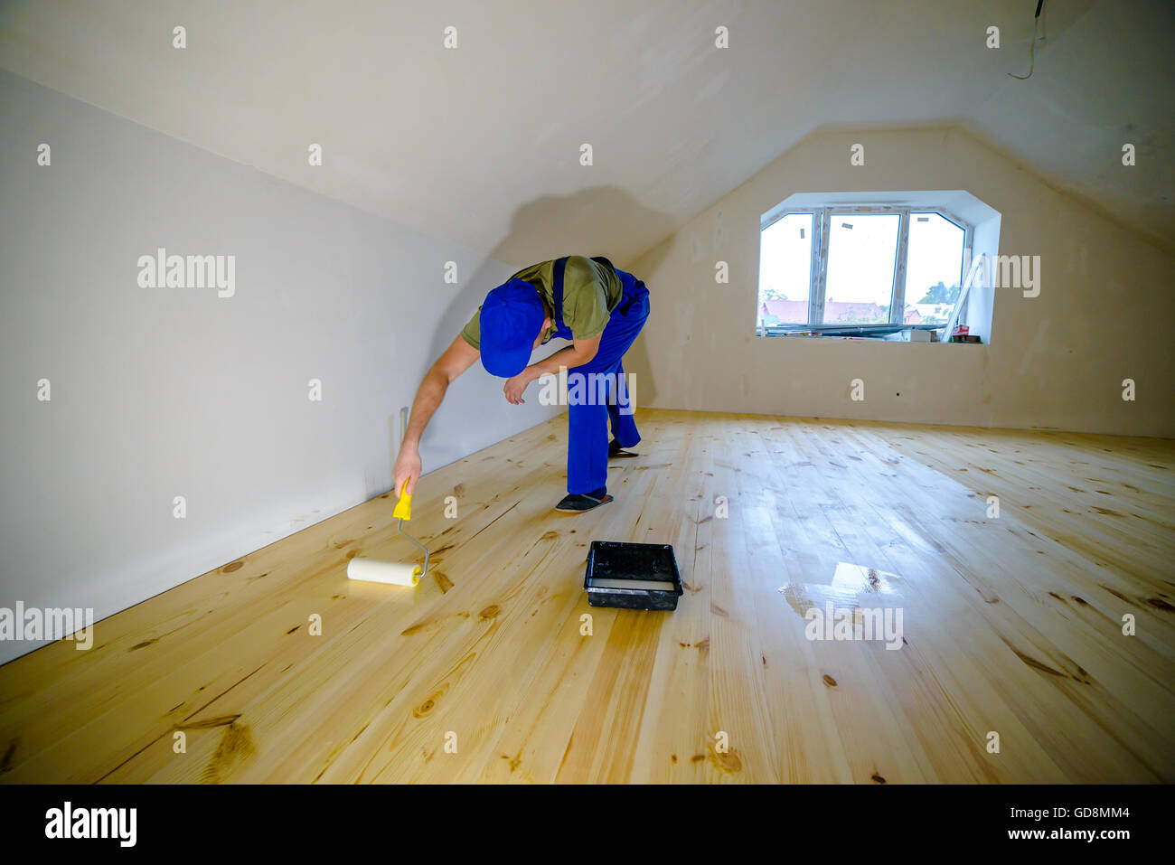 Wooden floor varnished. Worker with paint roller. Stock Photo