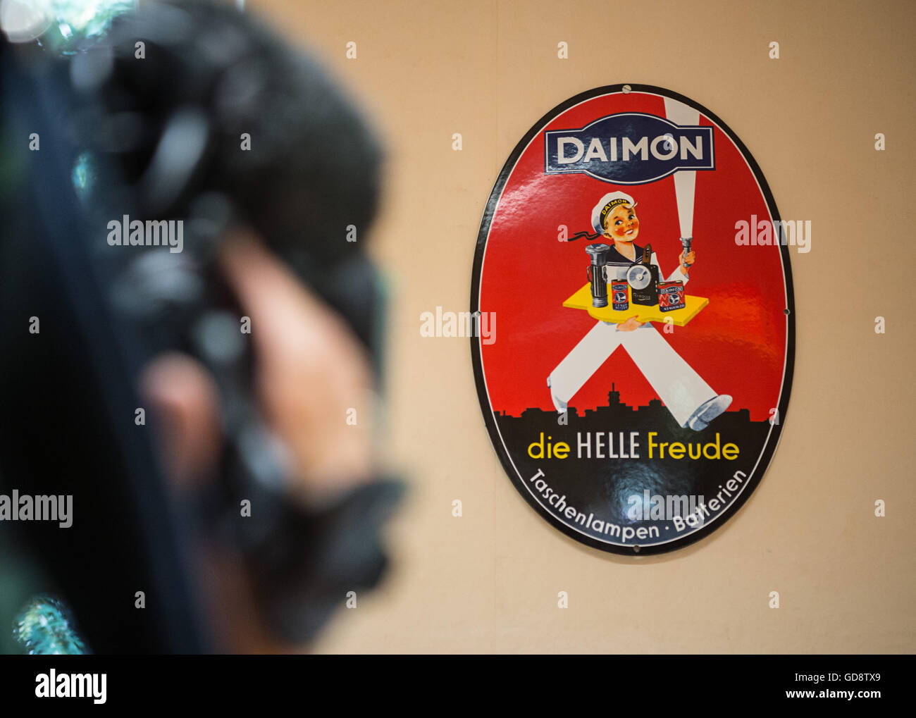 Berlin, Germany. 13th July, 2016. A cameraman films an old advertising board by the company Daimon at the opening of the Daimon Museum in Berlin, Germany, 13 July 2016. The museum is dedicated to the inventor of flashlights, Paul Schmidt, who also founded the company Daimon. Photo: Wolfram Kastl/dpa/Alamy Live News Stock Photo