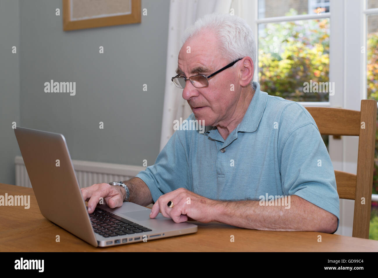 Old man sat down at a table using a laptop computer Stock Photo