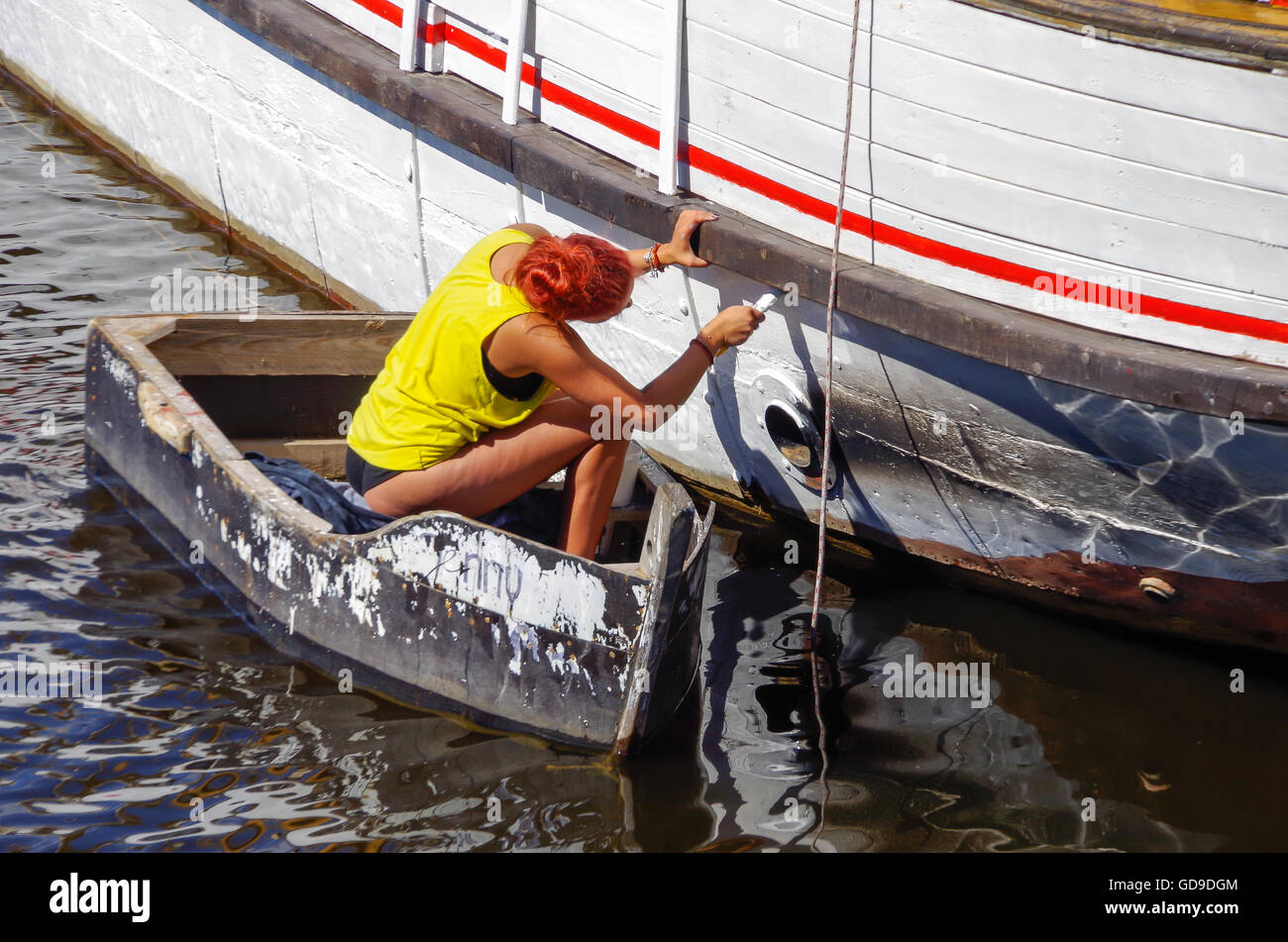 Red-haired girl in a yellow top painting a ship Stock Photo