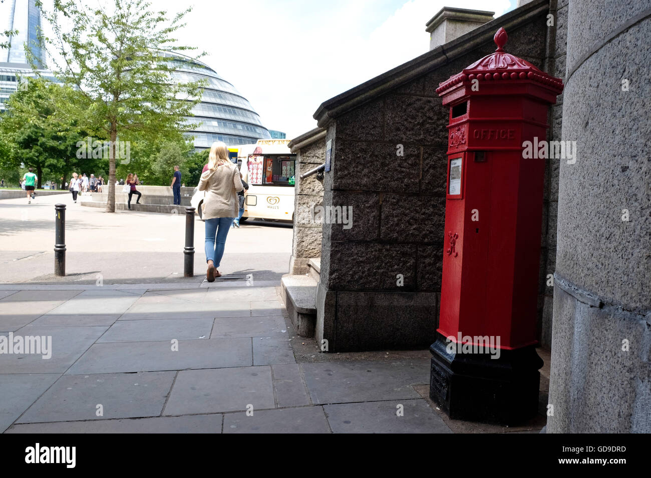 An iconic red British Mail letter box in London on the Thames walkway. London City Hall can be seen in the background Stock Photo