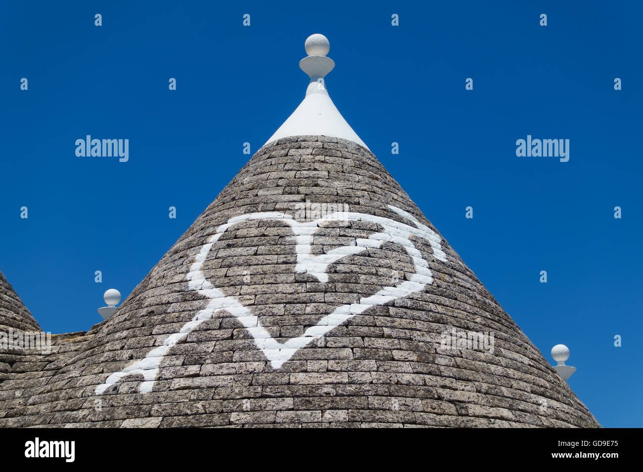 Detail of a stone trulli house roof with a heart painted on it in white paint in the town of Alberobello, Puglia, Italy. Stock Photo