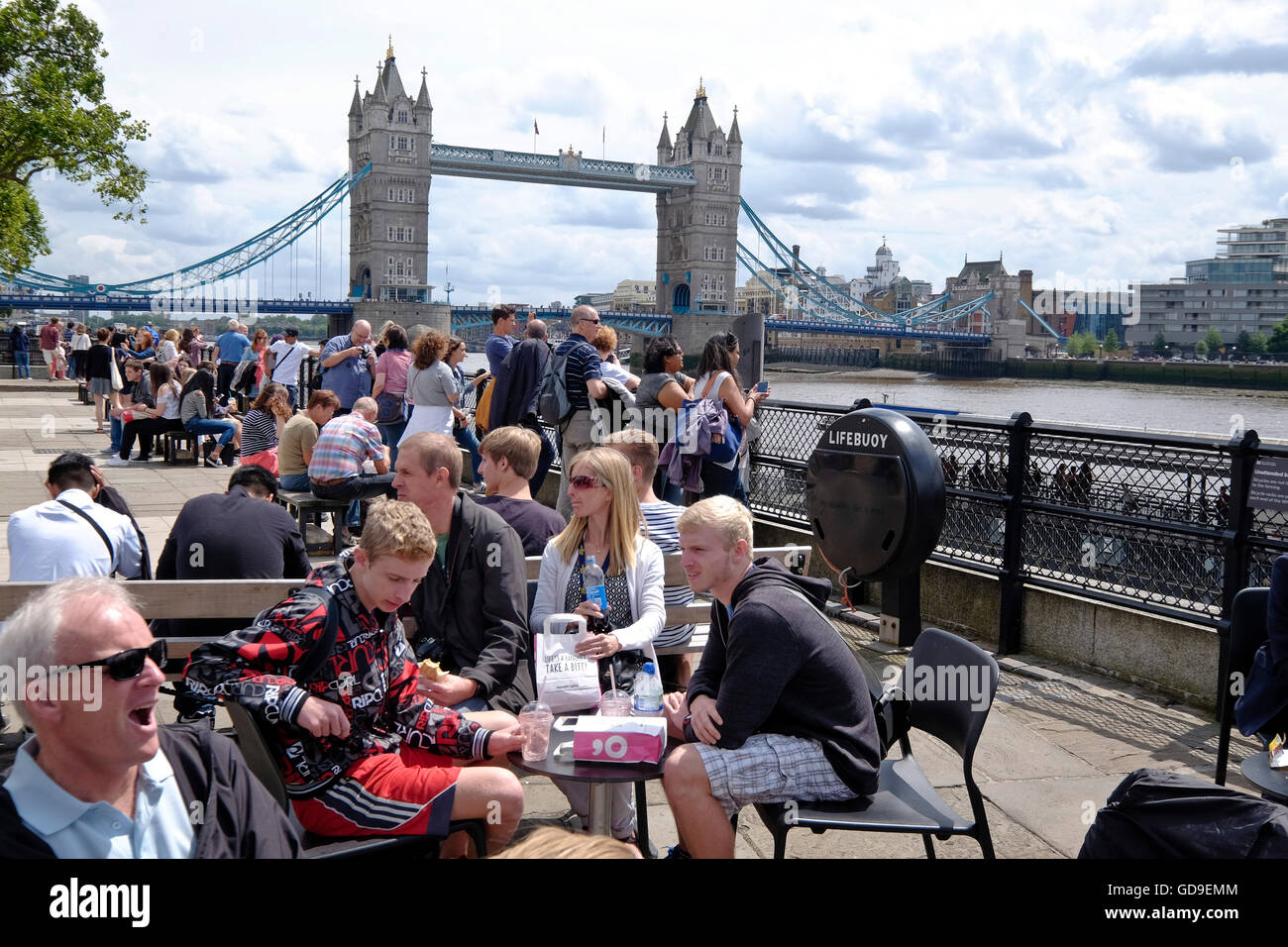 Tourists have lunch at an outdoor restaurant on Victoria Embankment along Thames River with the Tower Bridge and the London skyline in the background. Stock Photo