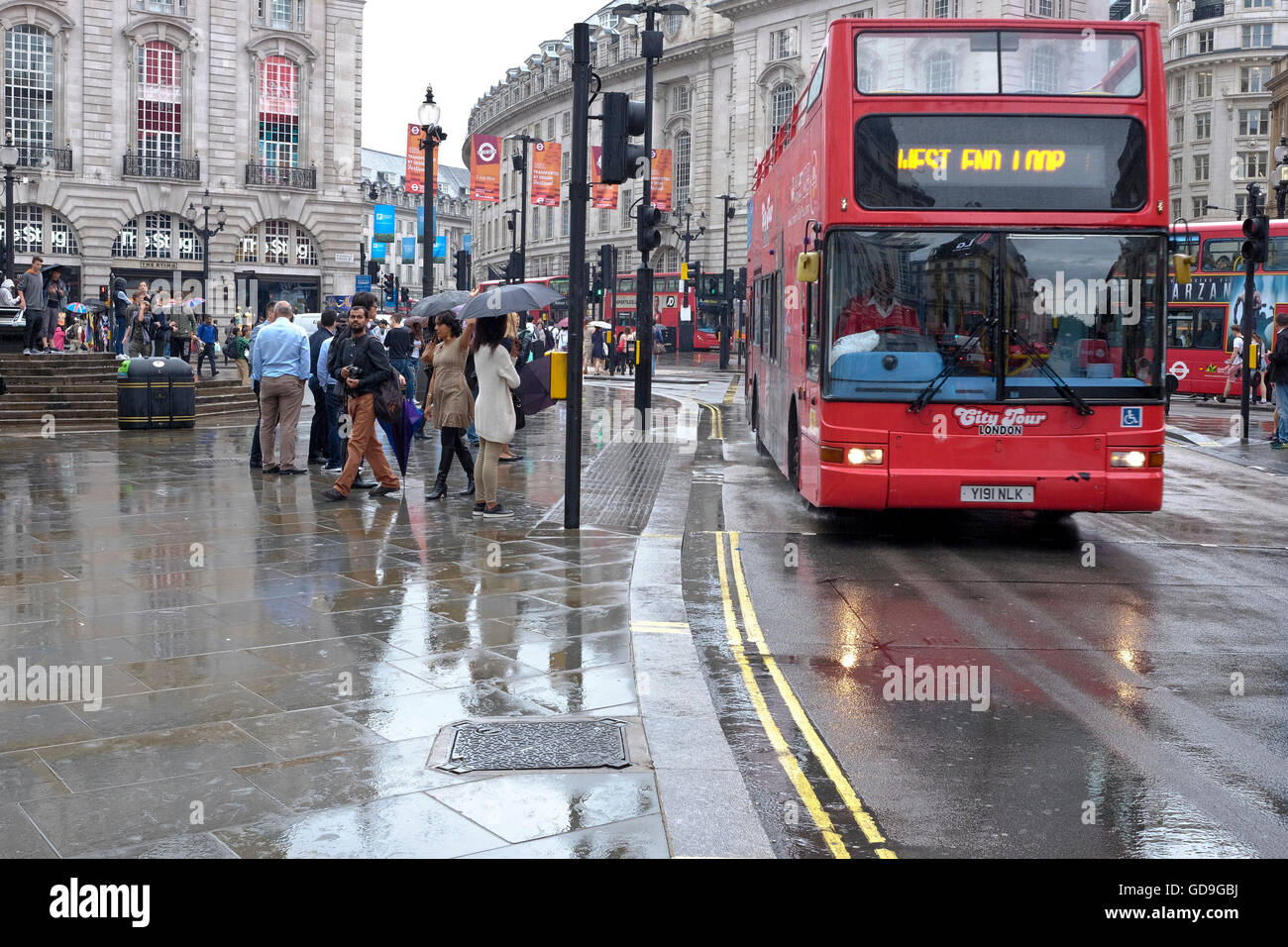 An iconic red London Bus traverses the wet road in Piccadilly Circus London Stock Photo