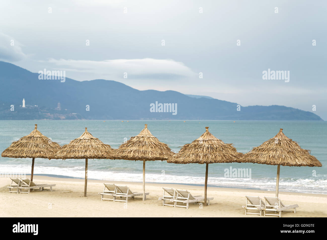 Palm shelters with sunbeds in the China Beach in Da Nang, Vietnam. It is also called NonNuoc Beach. South China Sea and Marble Mountains on the background. Stock Photo