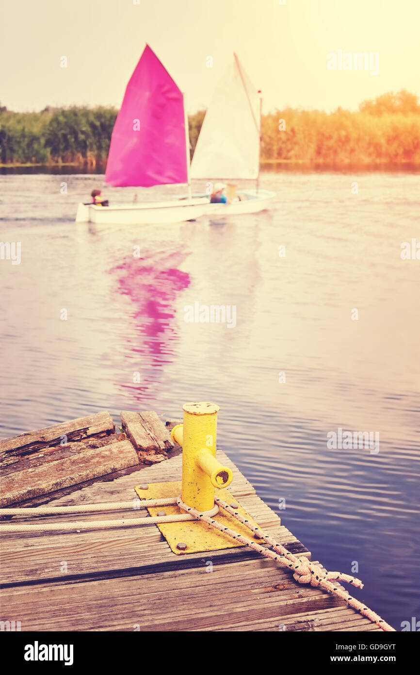 Vintage toned yellow mooring bollard on old wooden pier with sailboats in distance. Stock Photo