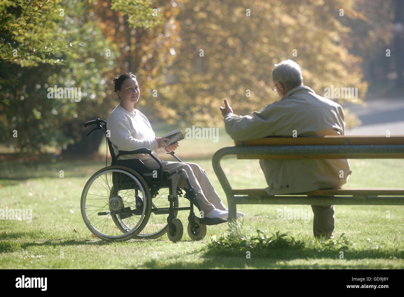 Woman sitting in a wheelchair, man sitting on a park bench Stock Photo ...