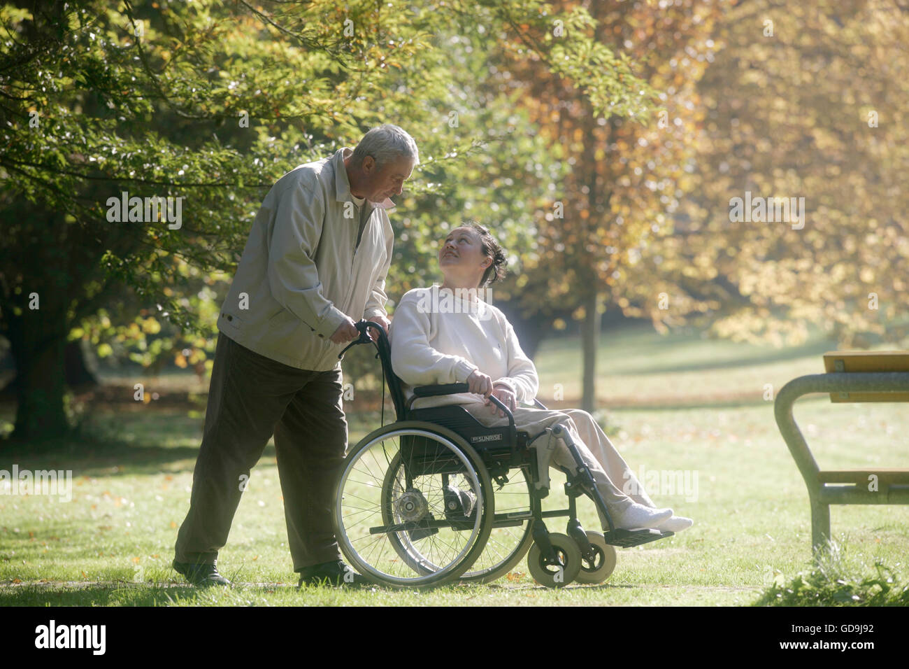 Man pushing awoman in a wheelchair in a park Stock Photo