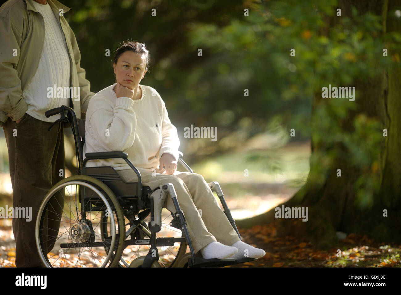 Woman is sitting in a wheelchair pensively, man standing next to her Stock Photo