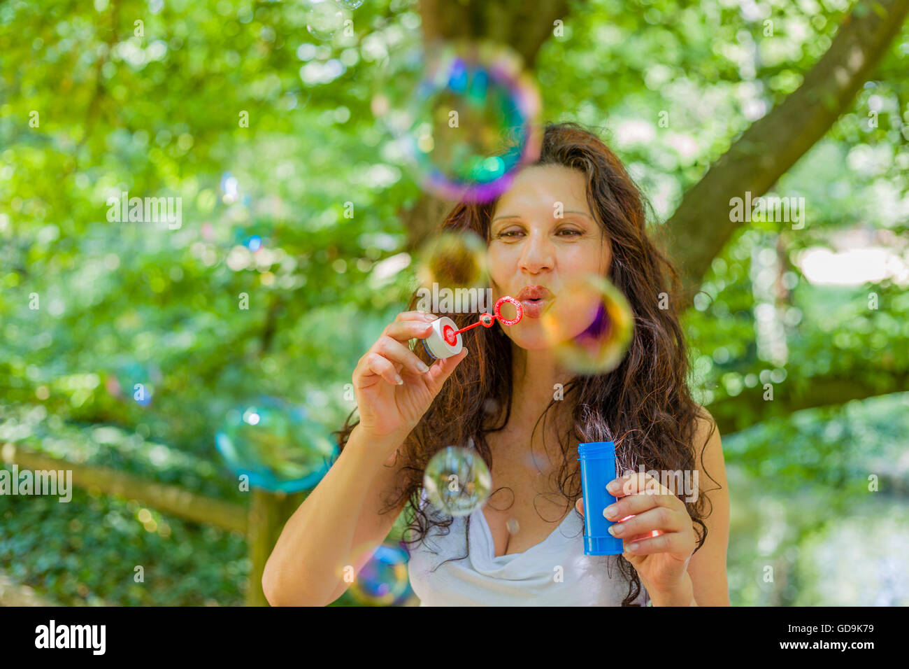 Fascinating mature adult woman is having fun like a child blowing soap bubbles in a public park Stock Photo