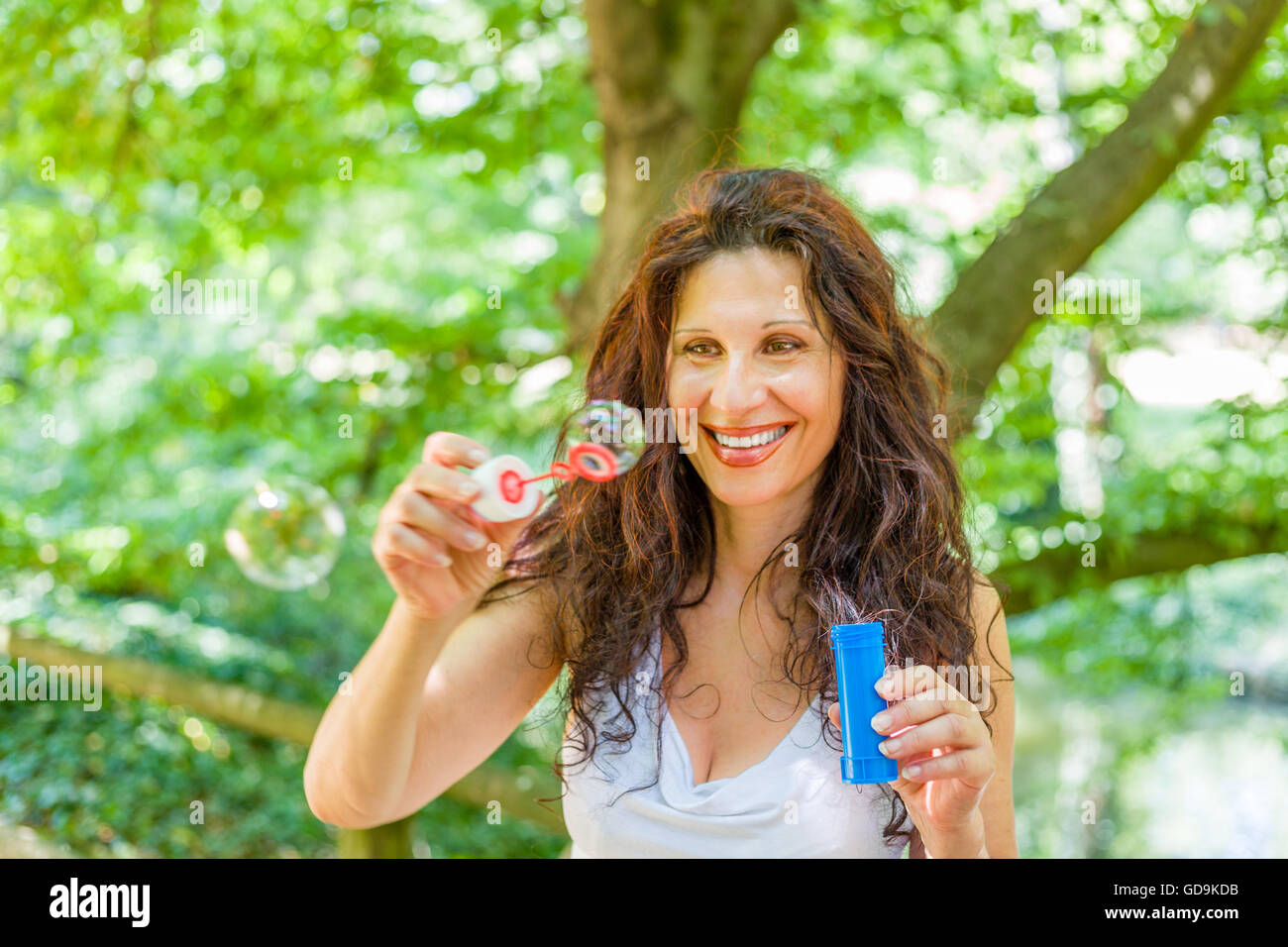 Fascinating mature adult woman is having fun like a child blowing soap bubbles in a public park Stock Photo
