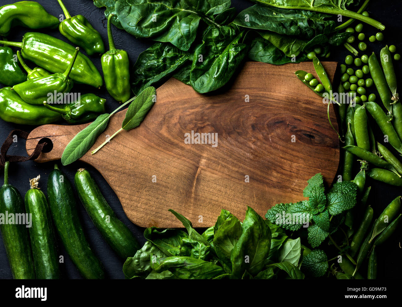 Fresh raw green vegetable ingredients for healthy cooking or salad making with dark wooden cutting baoard in center, top view, c Stock Photo