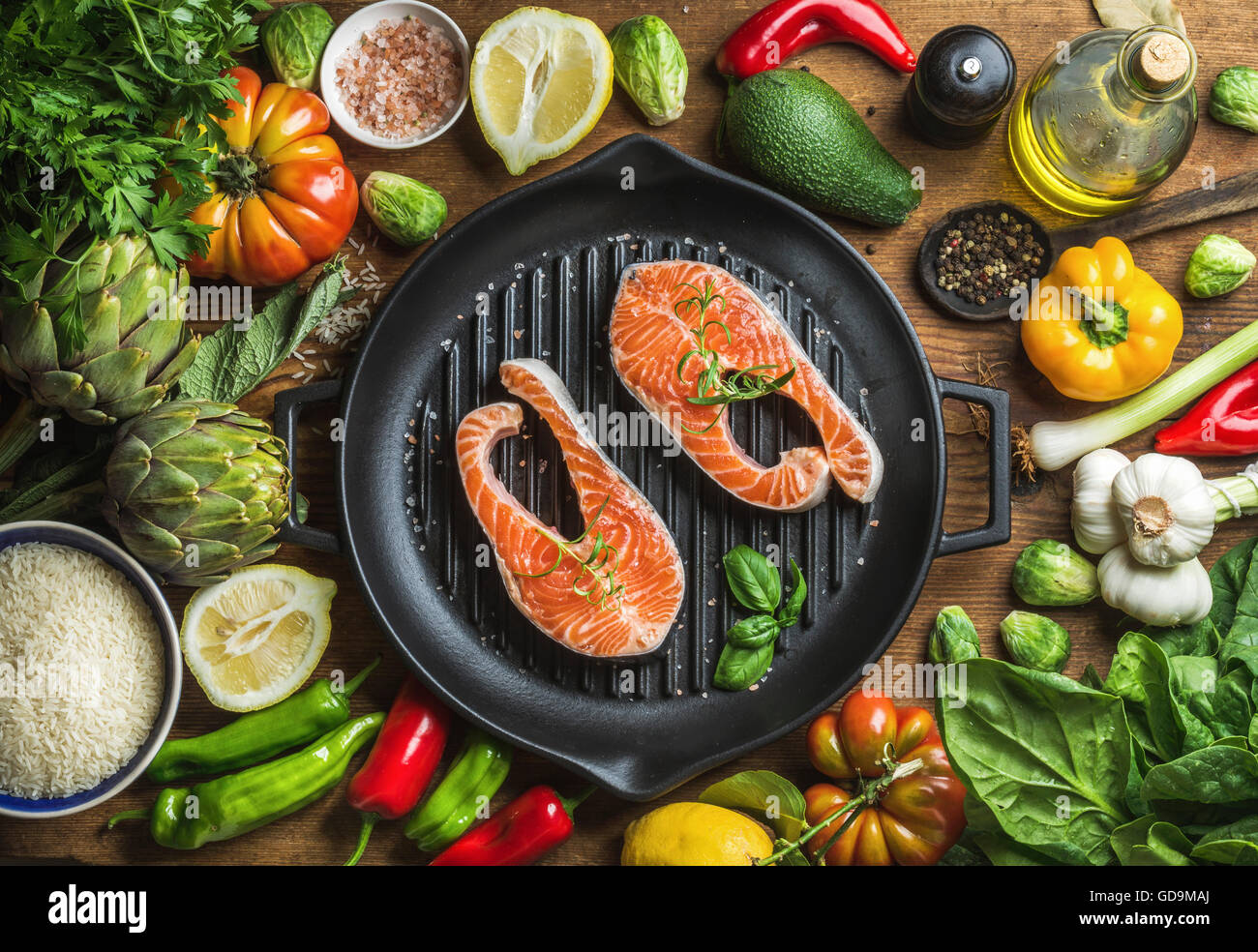 Raw uncooked salmon steakes with different vegetables, rice, herbs and spices on black grilling iron pan over rustic wooden back Stock Photo