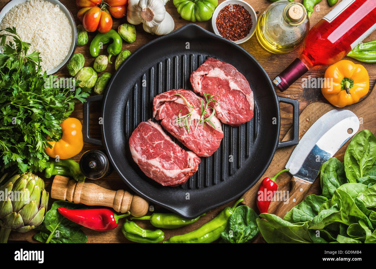 Ingredients for cooking healthy meat dinner. Raw uncooked beef steaks in cast iron grilling pan with vegetables, rice, spices, o Stock Photo