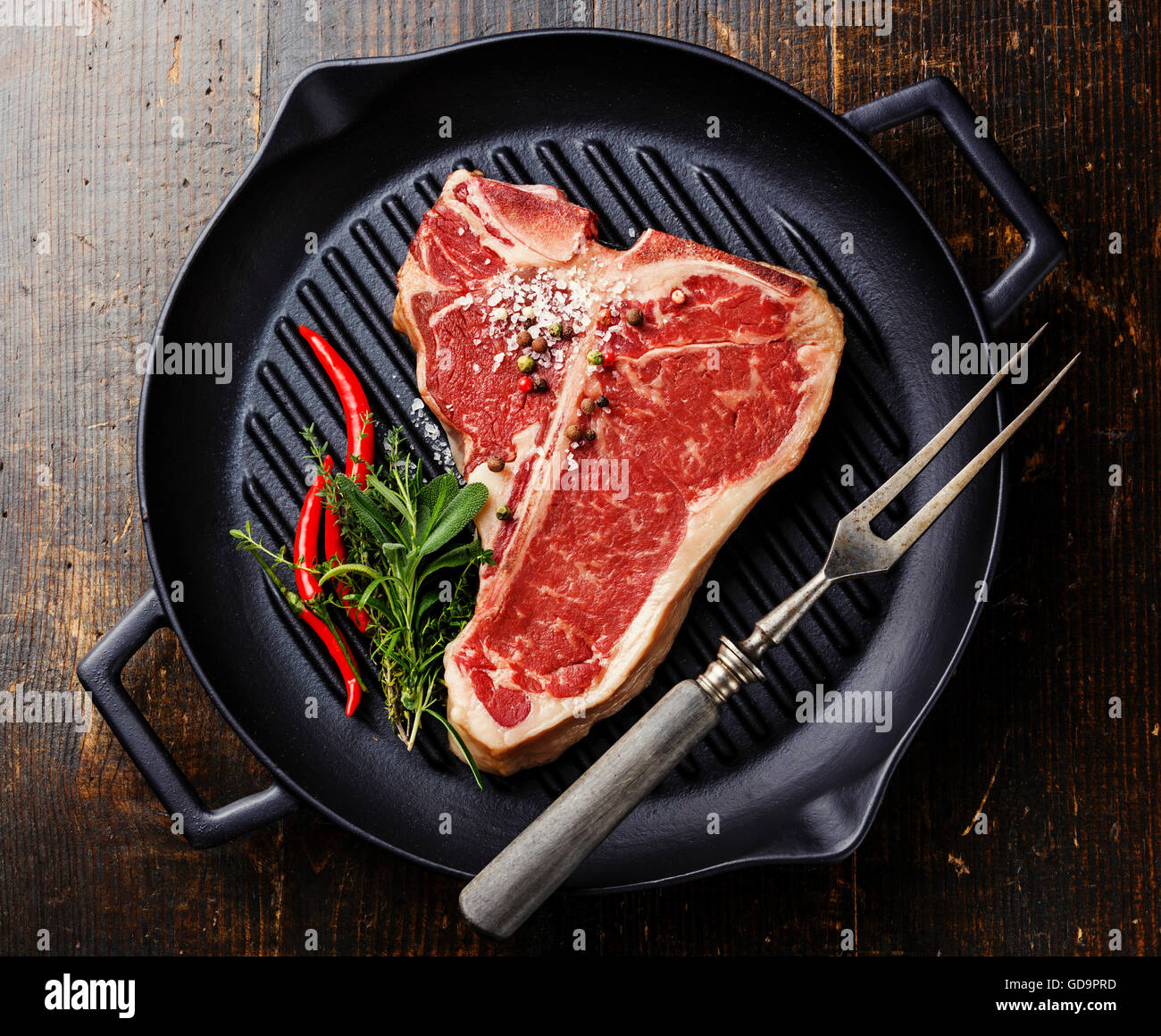 Raw fresh meat Tbone steak on grill iron pan, seasoning and Meat fork