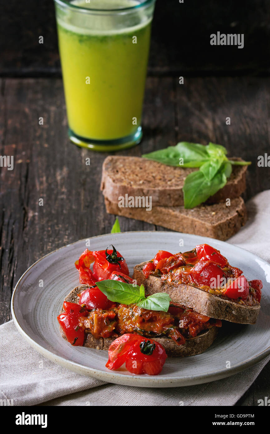 Italian tomato bruschetta with baked cherry tomatoes and fresh basil, served on gray ceramic plate with textile napkin and glass Stock Photo