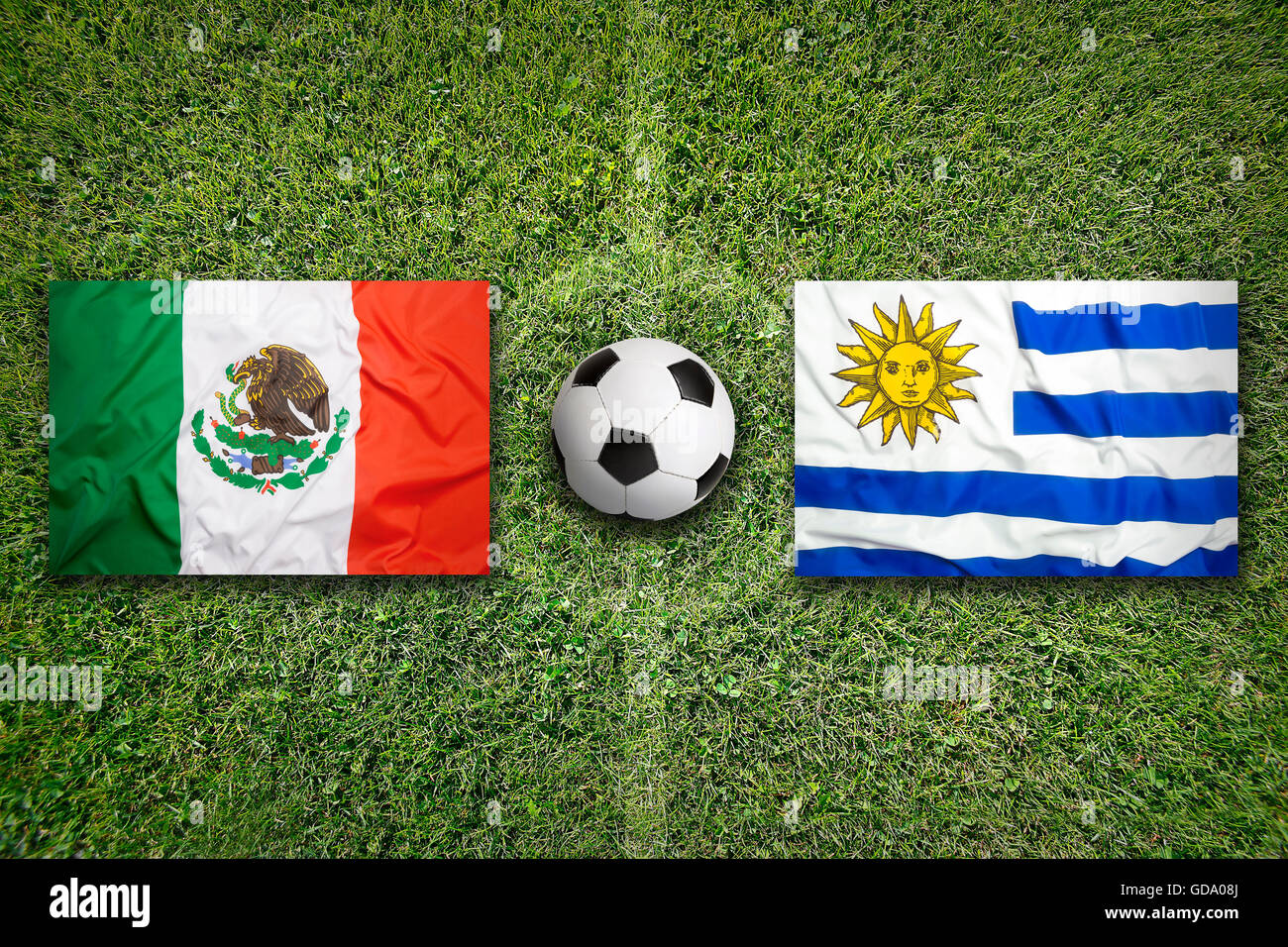 Mexico vs. Uruguay flags on green soccer field Stock Photo