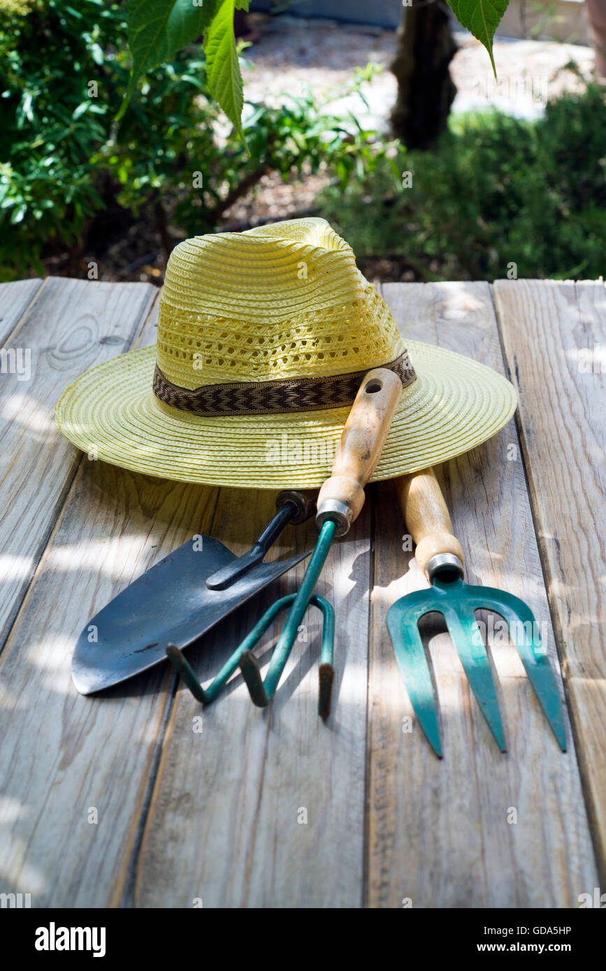 Basket of flowers, straw hat and gardening tools on wooden table Stock Photo