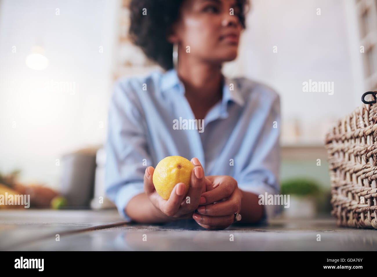 Close up shot of young woman standing at a juice bar counter holding lemon in her hand. Stock Photo