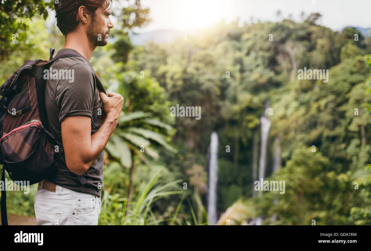 Side view shot of young man with backpack hiking in nature. Male hiker near waterfall in forest. Stock Photo