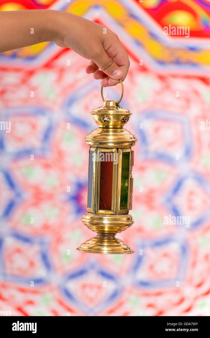 Hand with Small Ramadan Lantern over Ramadan Fabric Stock Photo