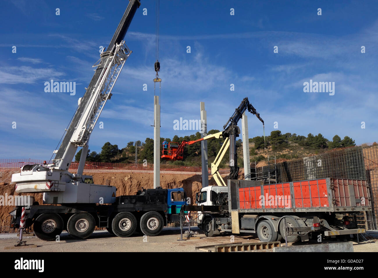 Construction site, cranes and trucks working with concrete pillars
