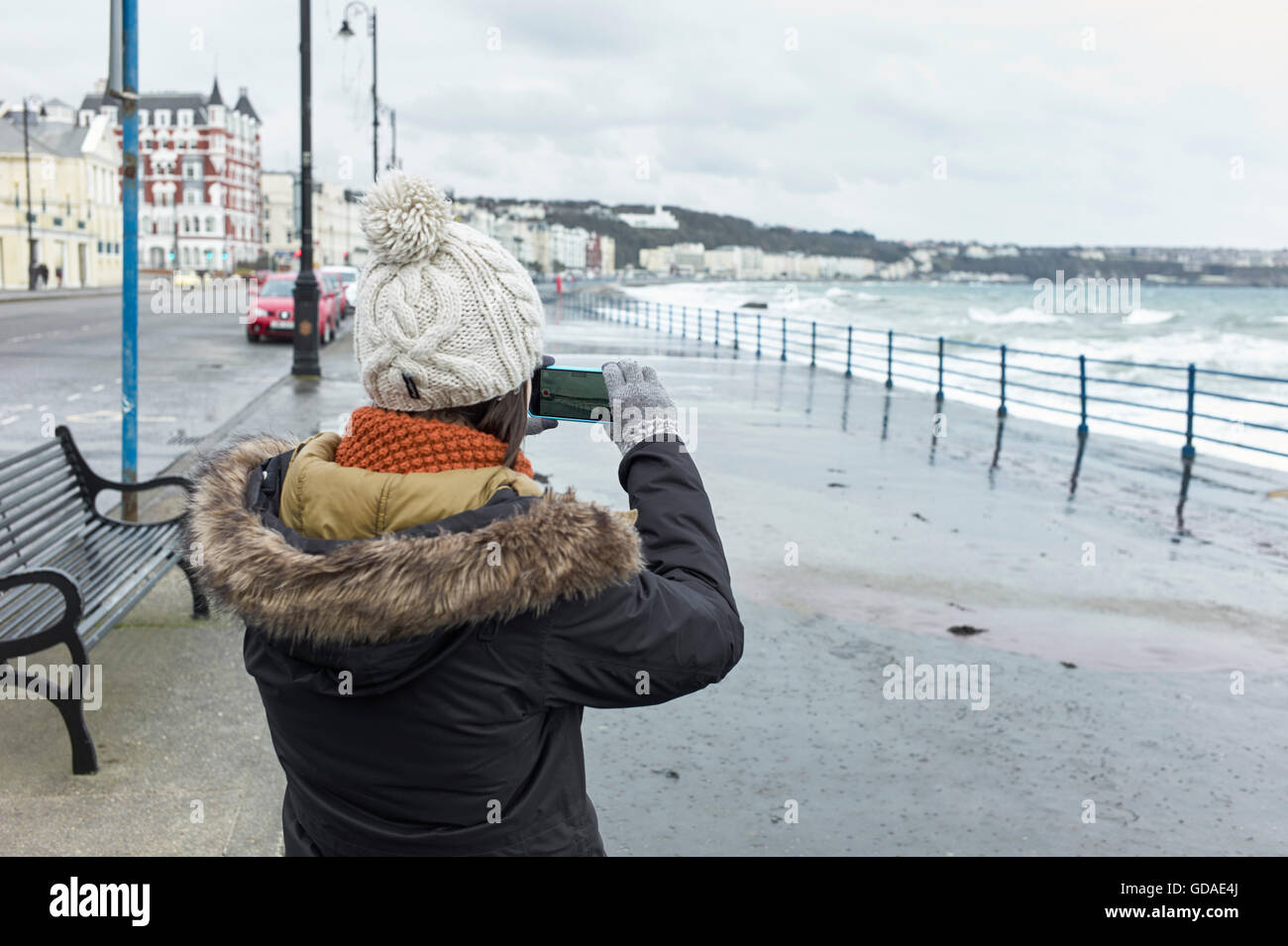 Young woman taking a photo on iphone at seaside in winter Stock Photo