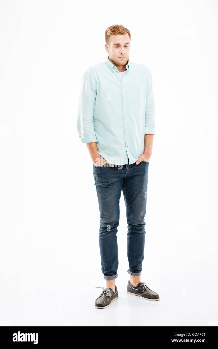 Full length of shy embarrassed young man standing with hands in pockets over white background Stock Photo