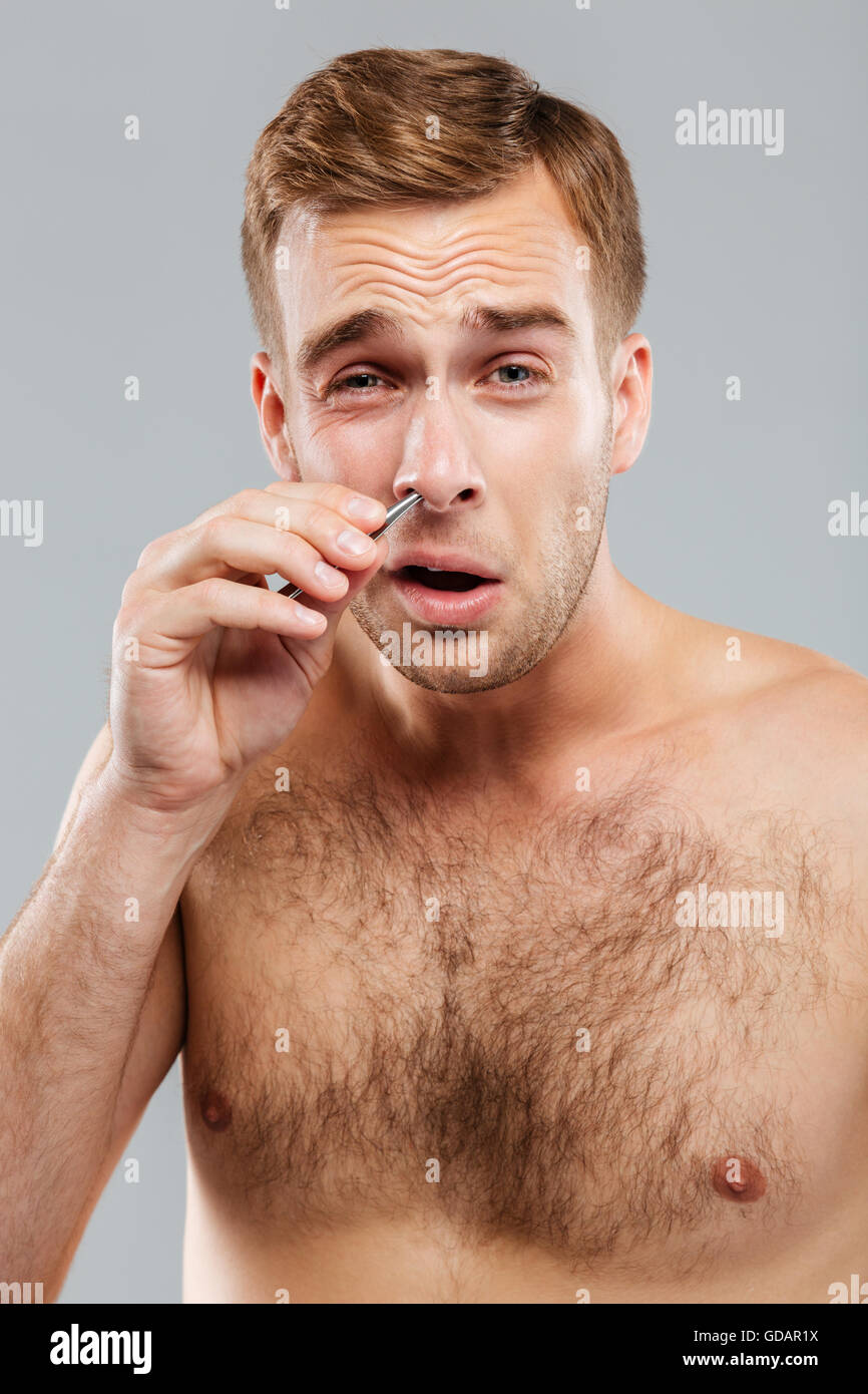 Closeup portrait of a man removing nose hair with tweezers isolated on the gray background