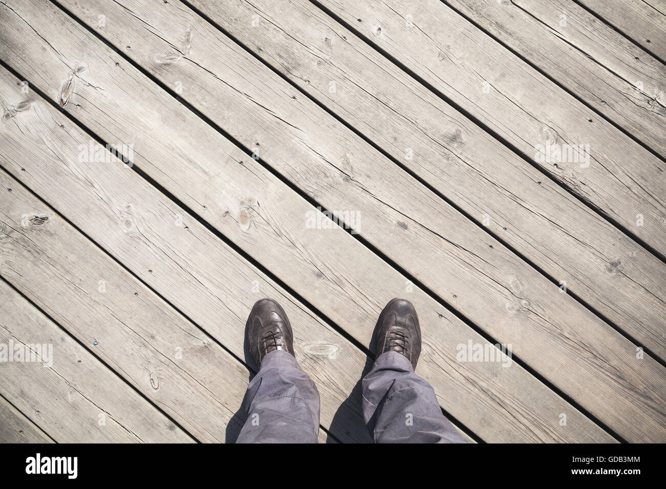 Male feet in leather shoes stand on old wooden pier floor, first person view Stock Photo
