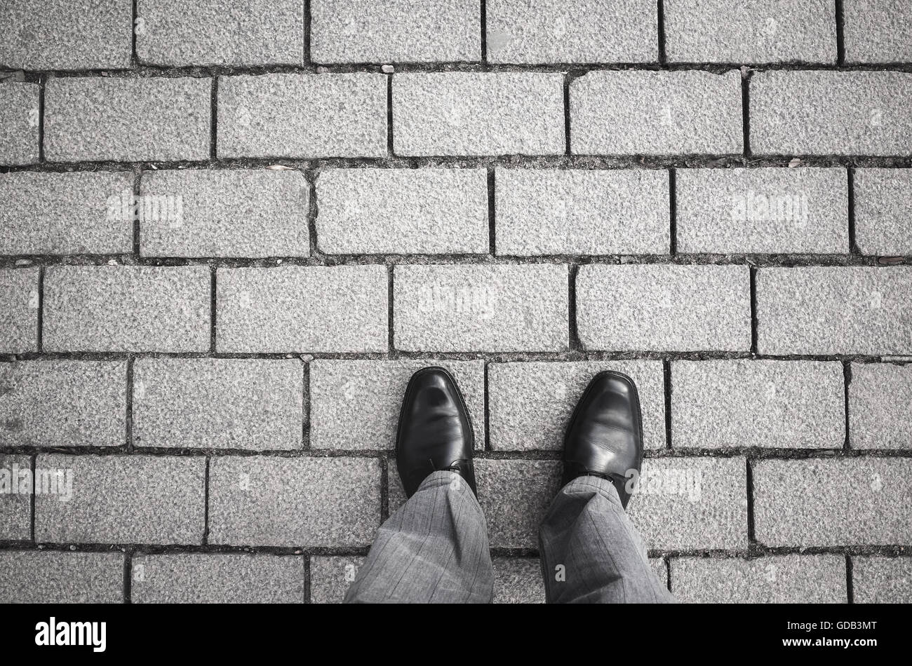 Feet of an urbanite man in black new shining shoes standing on gray cobblestone road Stock Photo