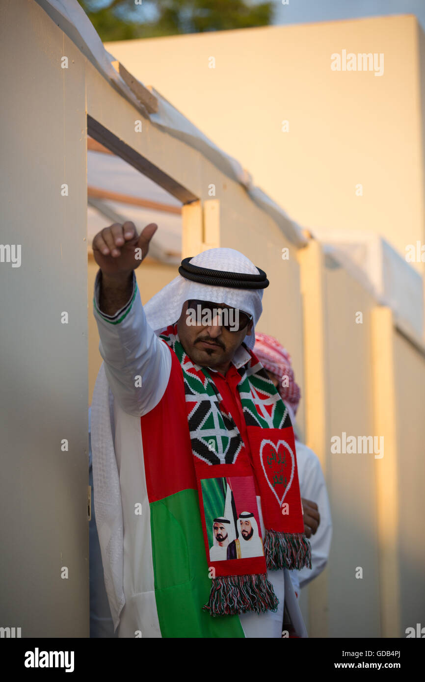 An Emirati man in a Kandura and a National Day scarf beckons someone