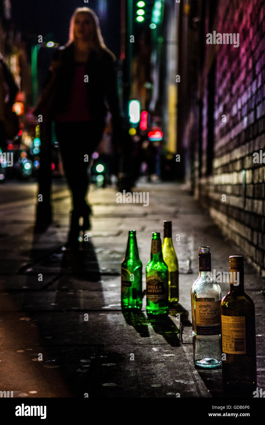 Late night shot of empty alcohol bottles on a street with city lights and people. Stock Photo