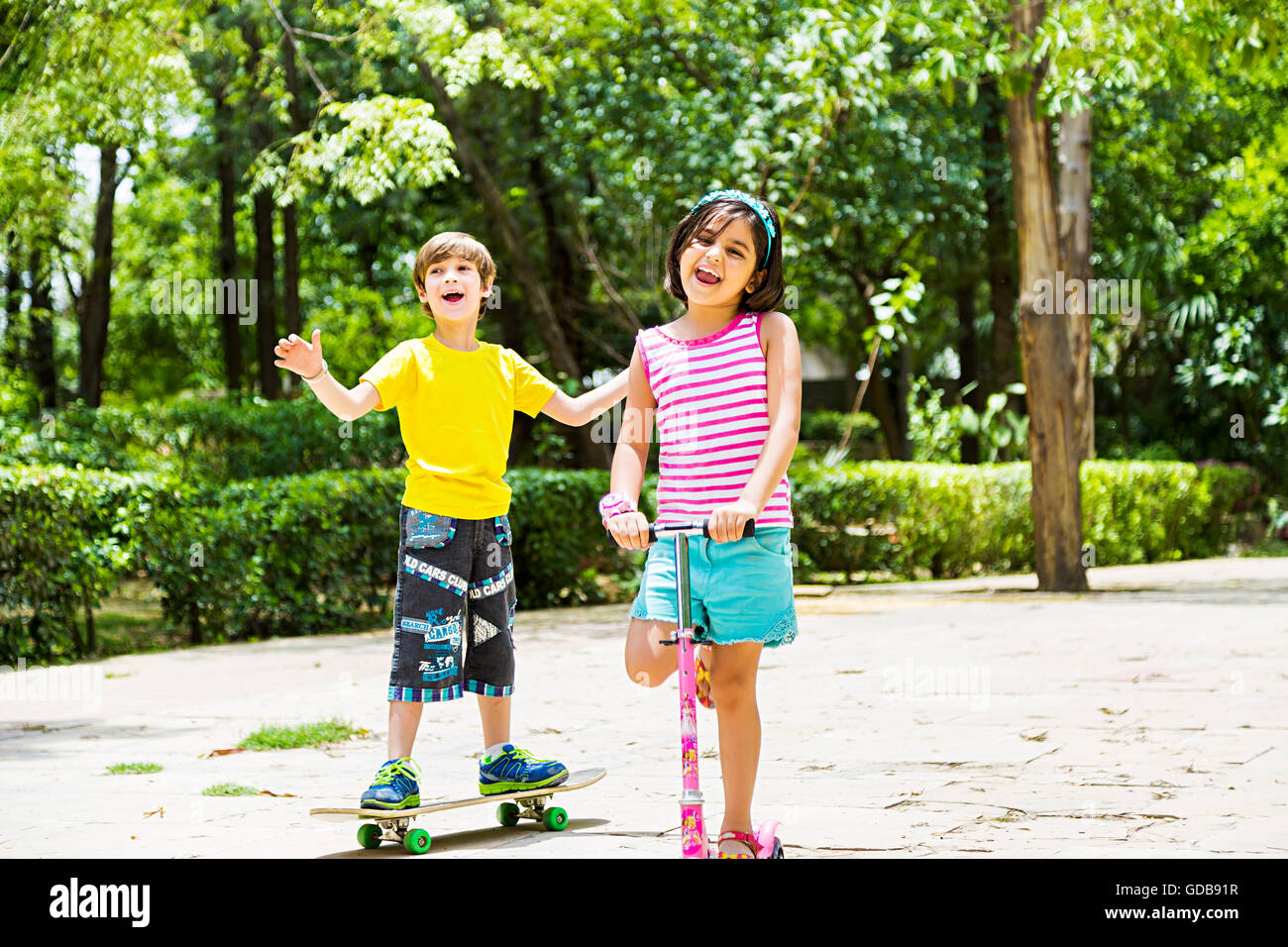 2 indians Kids boy and girl friends  Push Scooter Riding and Skateboard Skating Stock Photo