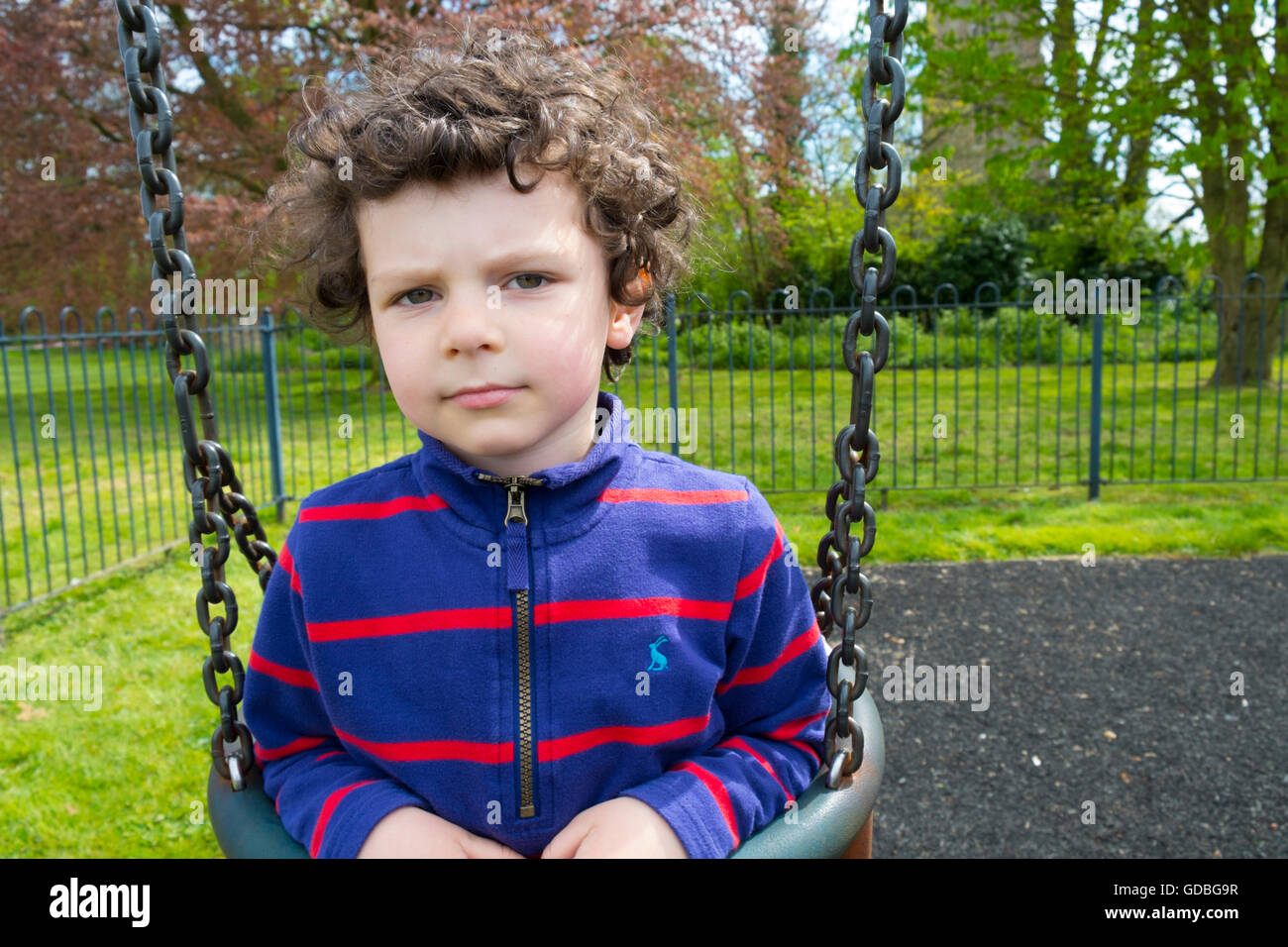 Young boy looking thoughtful on a playground swing Stock Photo