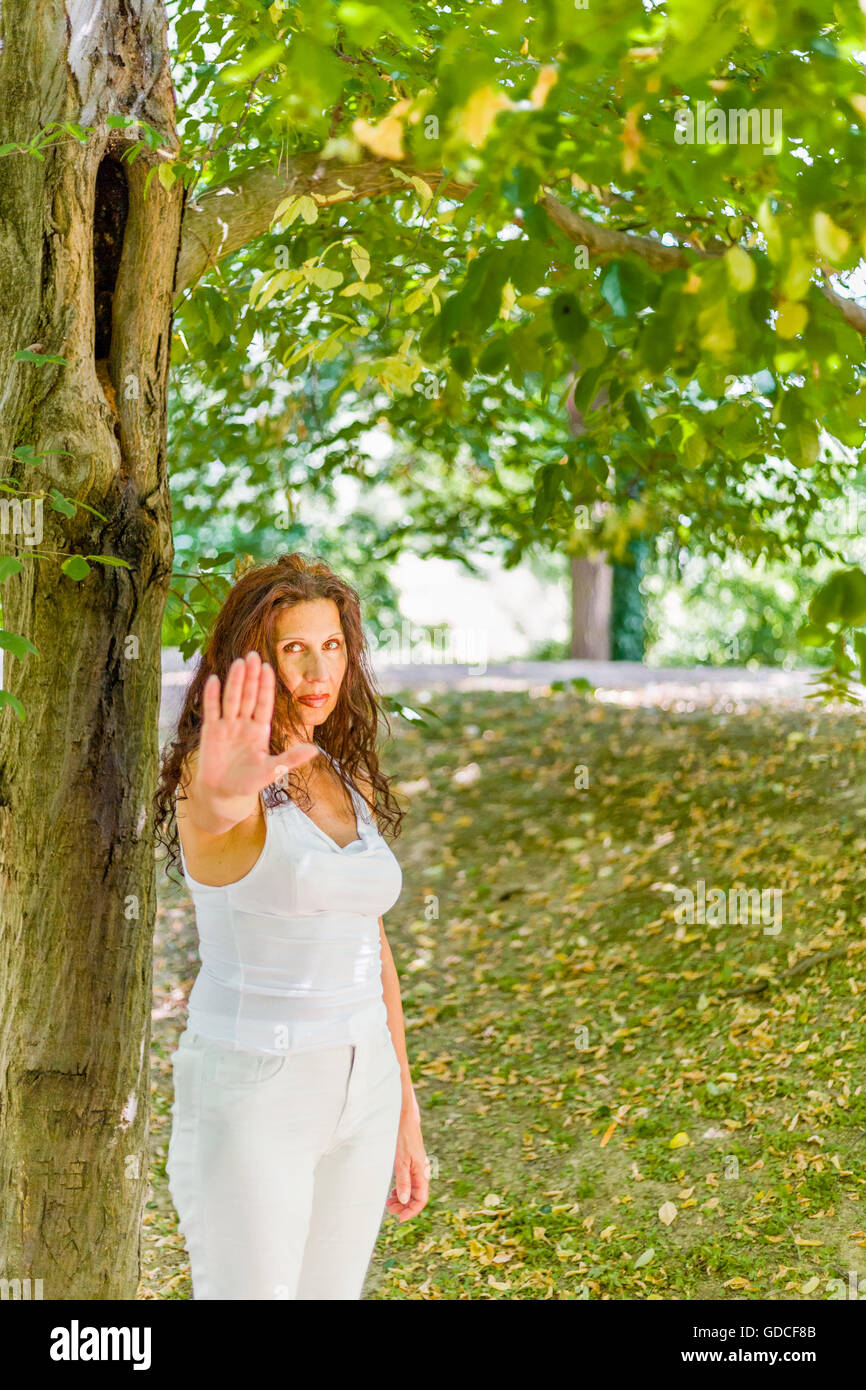 Stop and talk to my hand gesture by buxom over 40 woman with negative feelings against green garden background with copy space Stock Photo