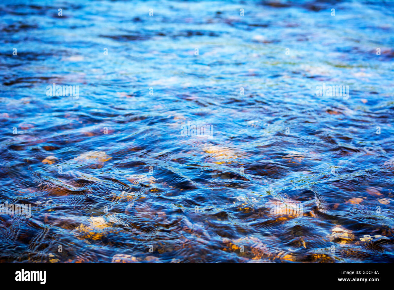 Defocused blue water surface background. Stony bottom of a clear mountain river. Flecks of sunlight and ripples on the water of Stock Photo