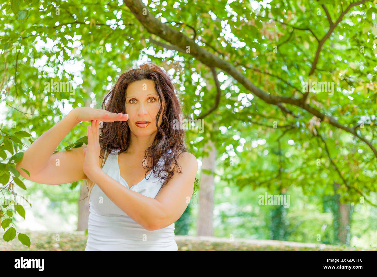 Buxom mature woman in white dress showing time out gesture, over green background Stock Photo