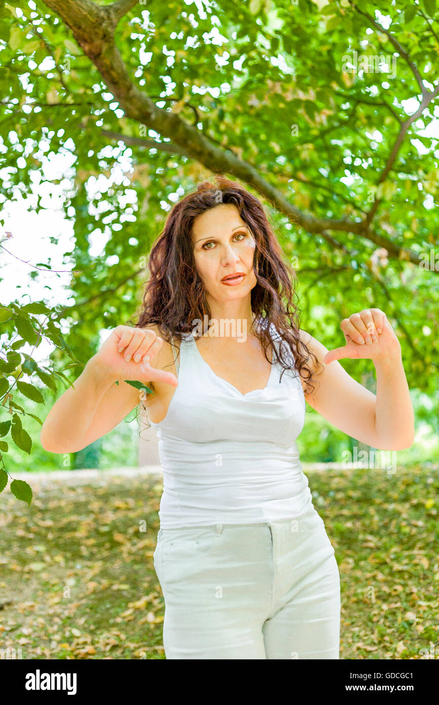 Unhappy busty classy mature woman giving thumbs down gesture looking with  negative expression at the camera against green garden background with copy  space Stock Photo - Alamy