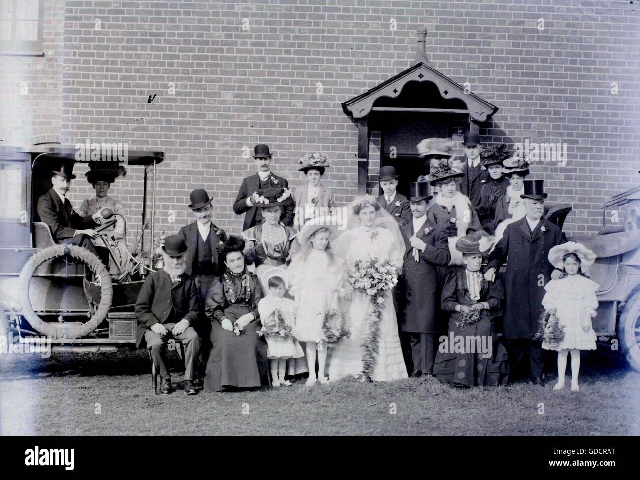 A formal wedding group photo, including motor cars in the Burton on