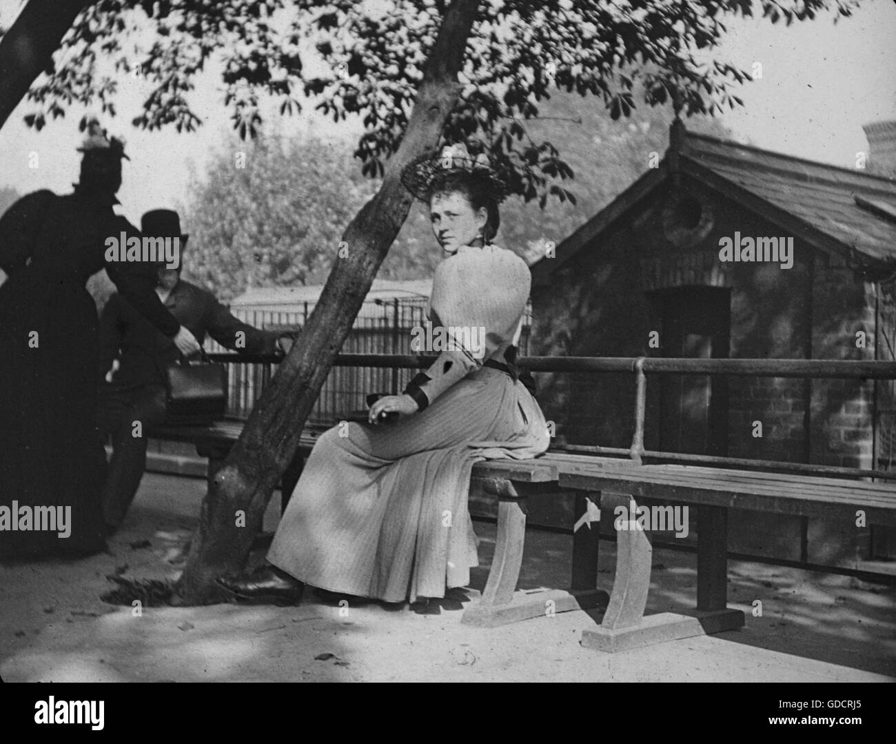 Candid portrait of a stunning young woman in hat and dress design with pooled natural lighting sitting on a bench. Amateur holiday photos c1899, venue appears to be Hastings. Photograph by Tony Henshaw - Taken from early original glass slides (original positive images). FROM THE 1899 HASTINGS FAMILY COLLECTION Stock Photo