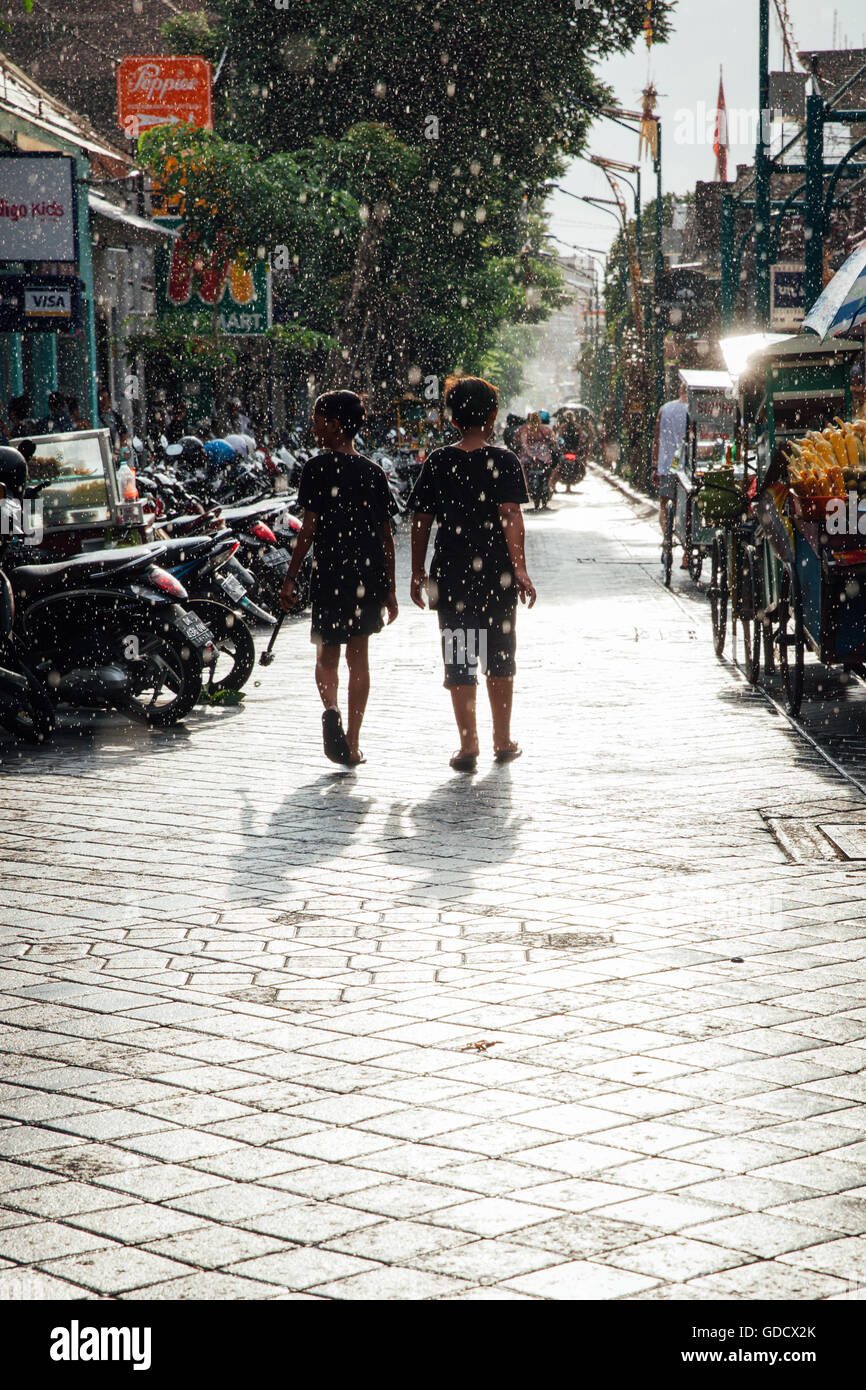 Kids walk under the sun shower on the street of Kuta, Bali, Indonesia on March 08, 2016 Stock Photo