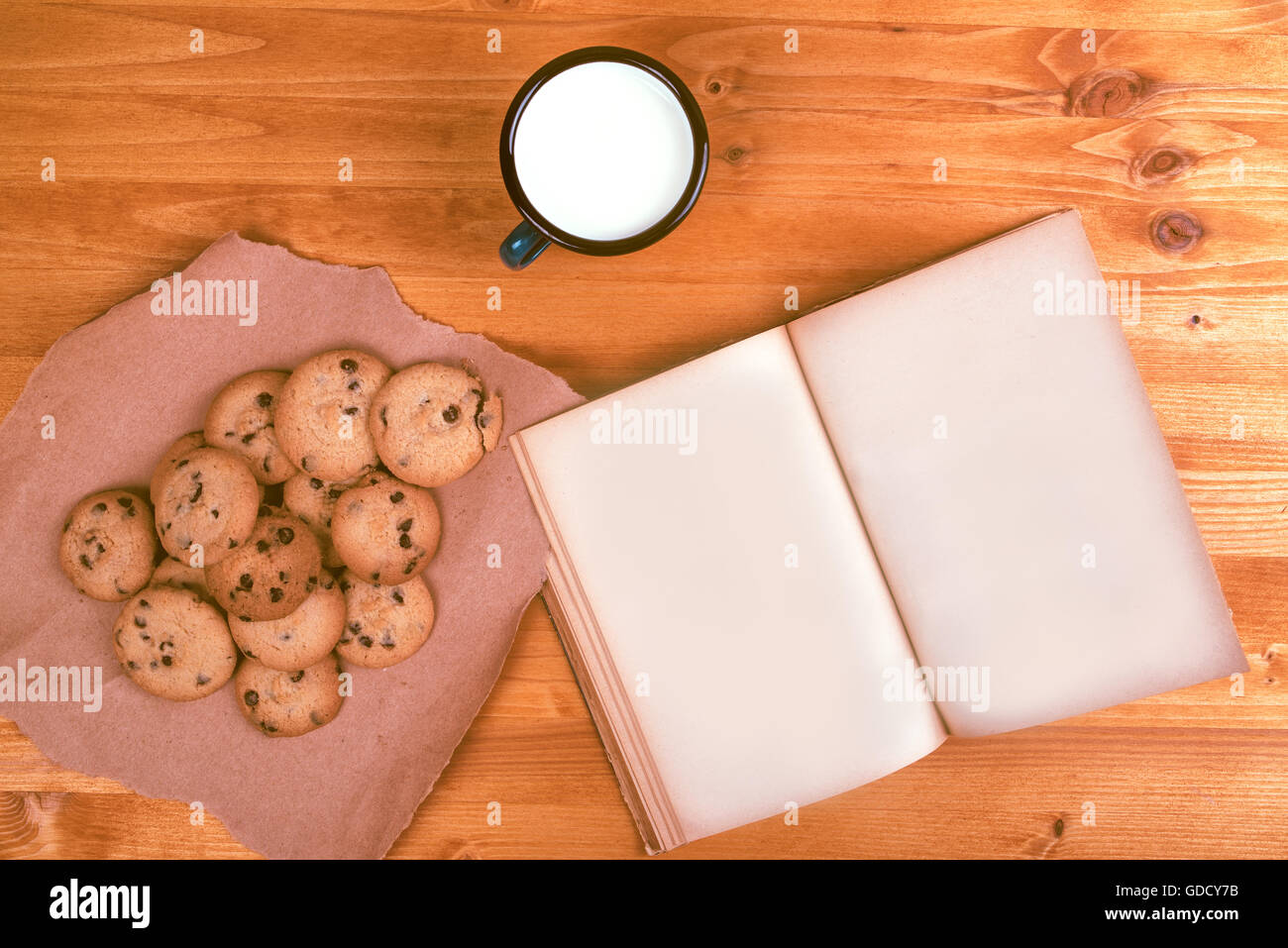 Homemade chocolate chip cookies, milk cup and open vintage recipe book on rustic wooden table, top view Stock Photo