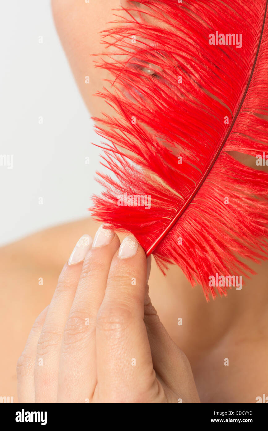 Woman hiding face with a red feather Stock Photo - Alamy
