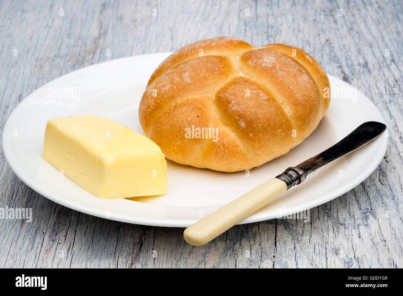 Bread roll butter & knife on a plate served outdoors on the picnic table. Stock Photo