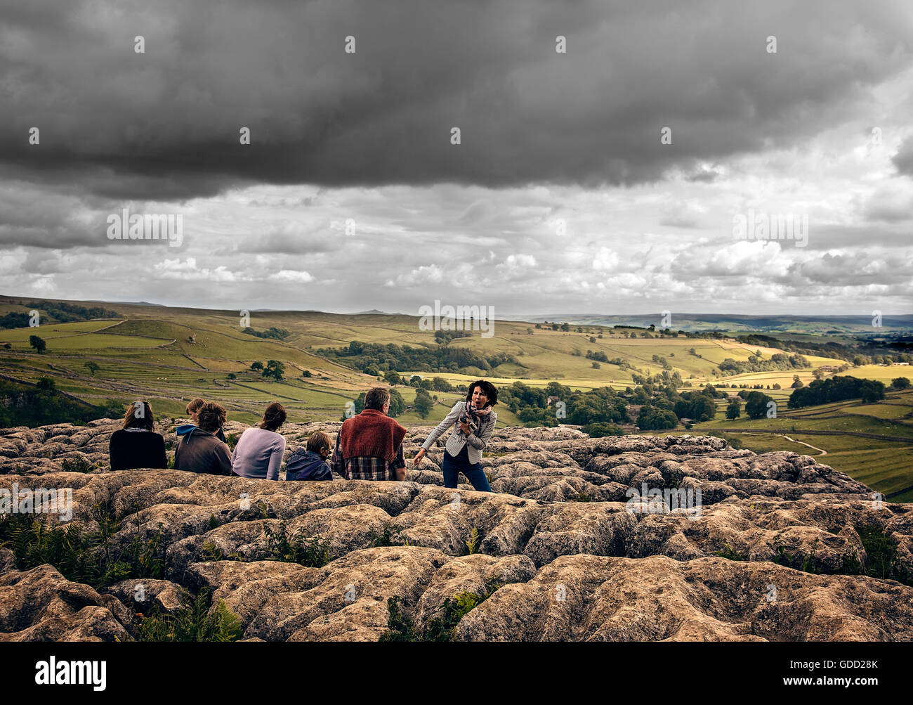 Group of people on Malham Cove enjoying the view as the rain begins.  Family sitting on rocks outdoors for rainy picnic with dark skies on the horizon Stock Photo