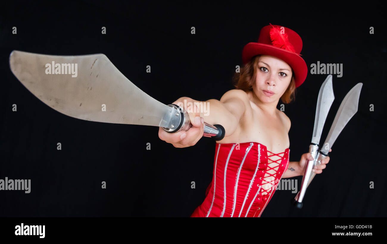 Knife juggler in red basque and top hat holding out one of her knives