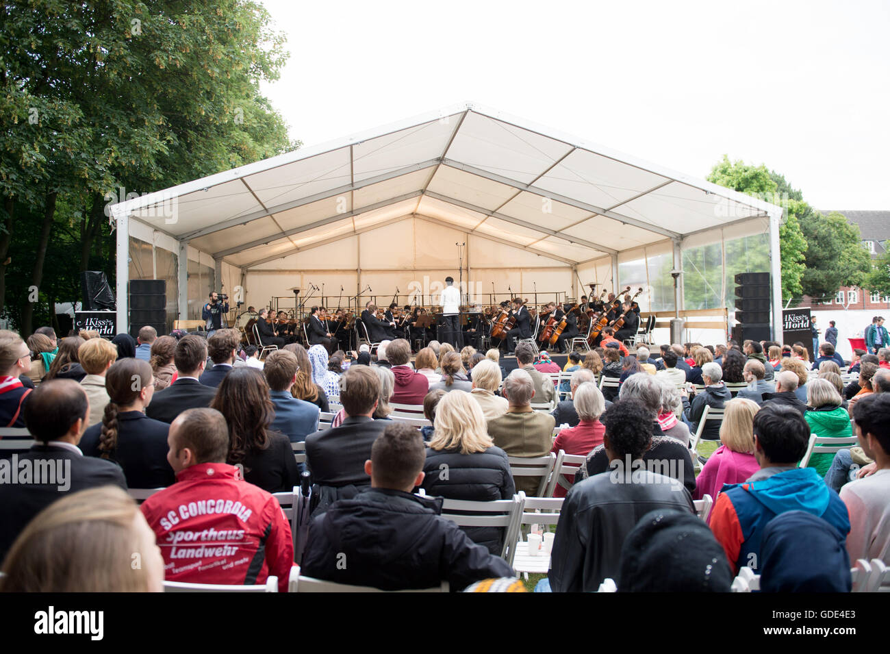 Hamburg-Osdorf, Germany. 15th July, 2016. The Hamburg Symphony Orchestra give an open air concert for refugees, volunteers and neighbours at a reception camp in Hamburg-Osdorf, Germany, 15 July 2016. Among other things, the orchestra played the 9th symphony by Beethoven. Photo: Daniel Reinhardt/dpa/Alamy Live News Stock Photo